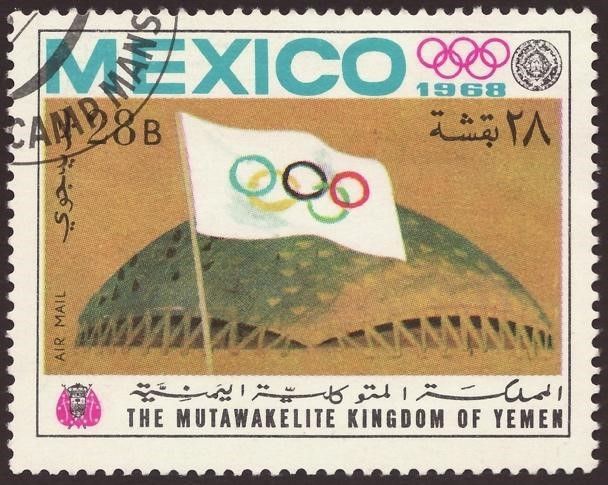 طابع للملكة المتوكلية اليمنية، 1968، يصور علم الأولمبياد أمام قصر الرياضات، الصورة مقتبسة من ويكيميديا كومونز. 