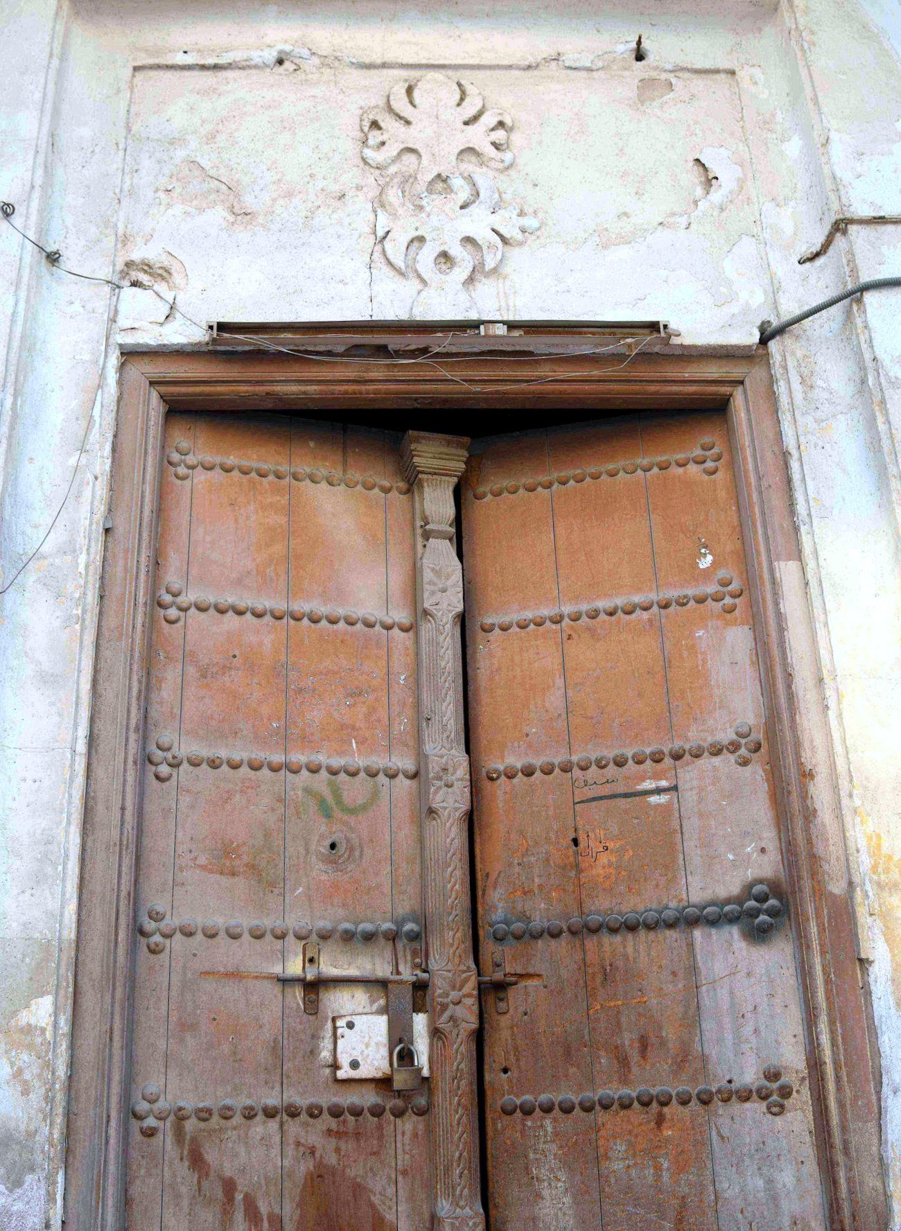 صفوف من المسامير المجدولة بما يشبه السلسلة في إطار الباب ونقش ورقة التين المُدرج في خشم "بو جُرو" في الأحساء. بإذن من د. سعيد الوايل.&nbsp;